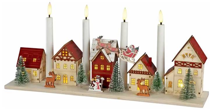 Oplyst julelandsby-display med fem miniaturhuse, fire stearinlys, små træer og festlige figuriner på en træbase.