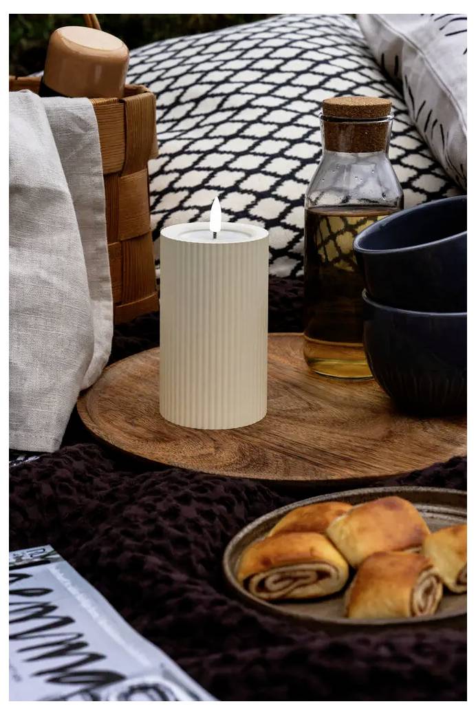 Morgenbordservice med lys på en seng med bagværk, te, kopper og en glasflaske i en hyggelig, mønstret indretning.