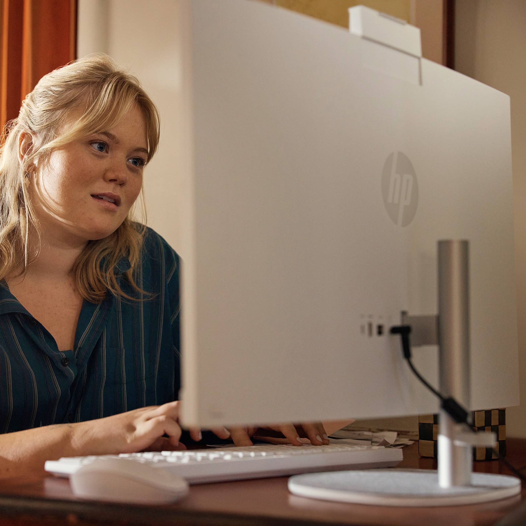 Kvinde, der arbejder ved en stationær computer, set fra bag skærmen, i et hjemmekontor.