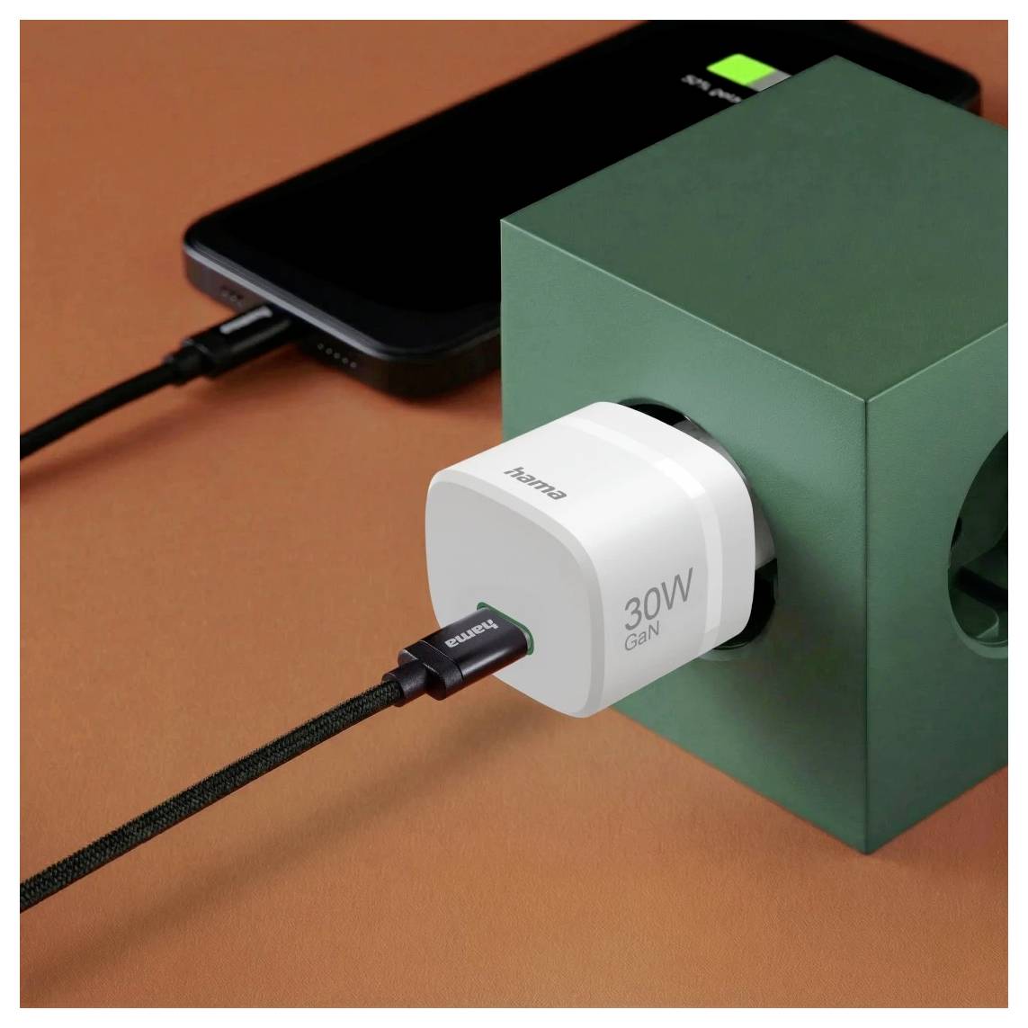 Hvid 30W GaN-oplader tilsluttet til en grøn kube, der lader en smartphone op med flettet USB-C-kabler på en orange overflade.