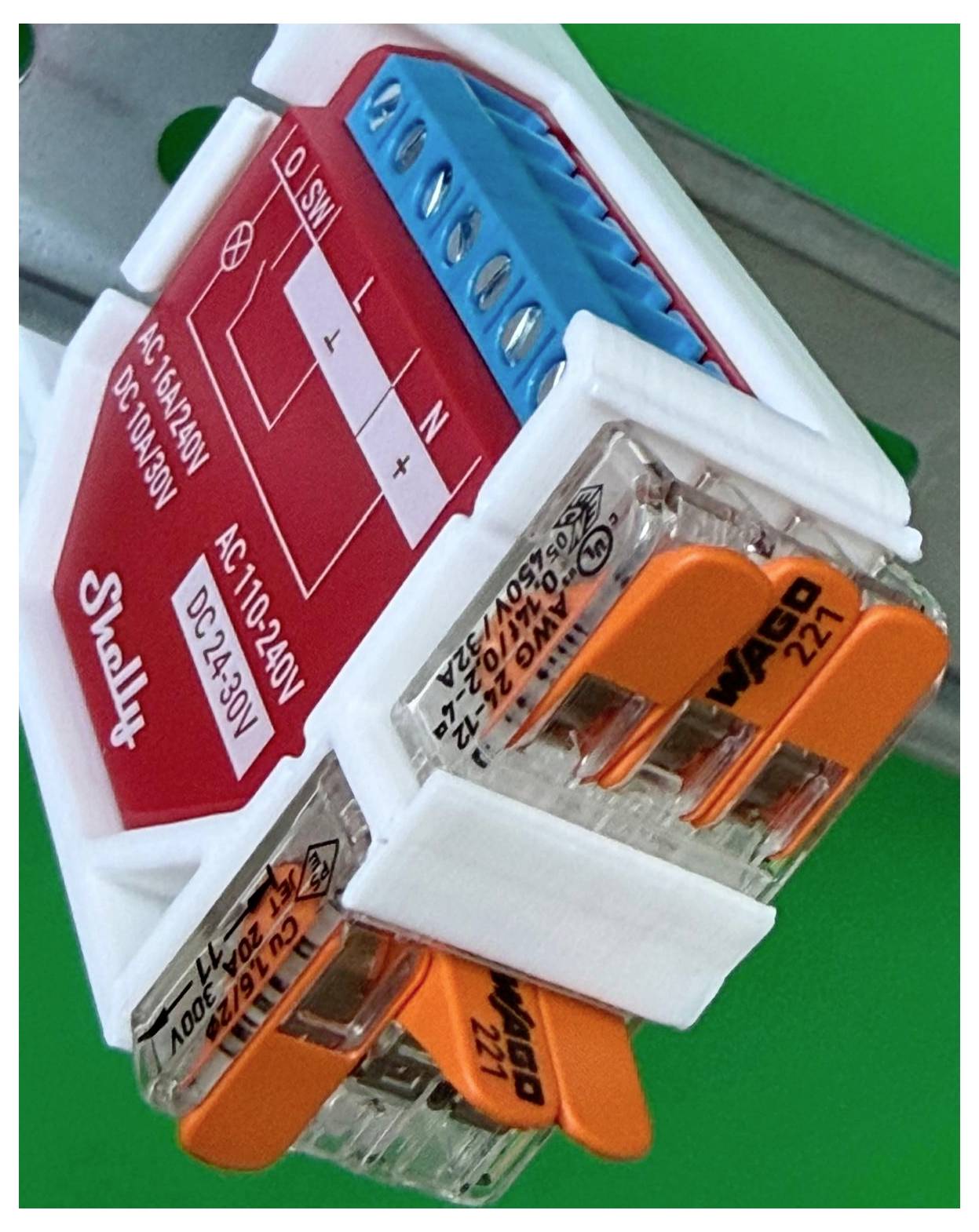 Detaljeret billede af et kompakt elektrisk kontaktmodul med røde og blå terminaler og orange stikforbinder på grøn baggrund.