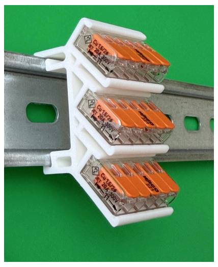 Tre orange-og-gennemsigtige elektriske stikforbindelser klippet på en metal monteringsskinne mod en grøn baggrund.