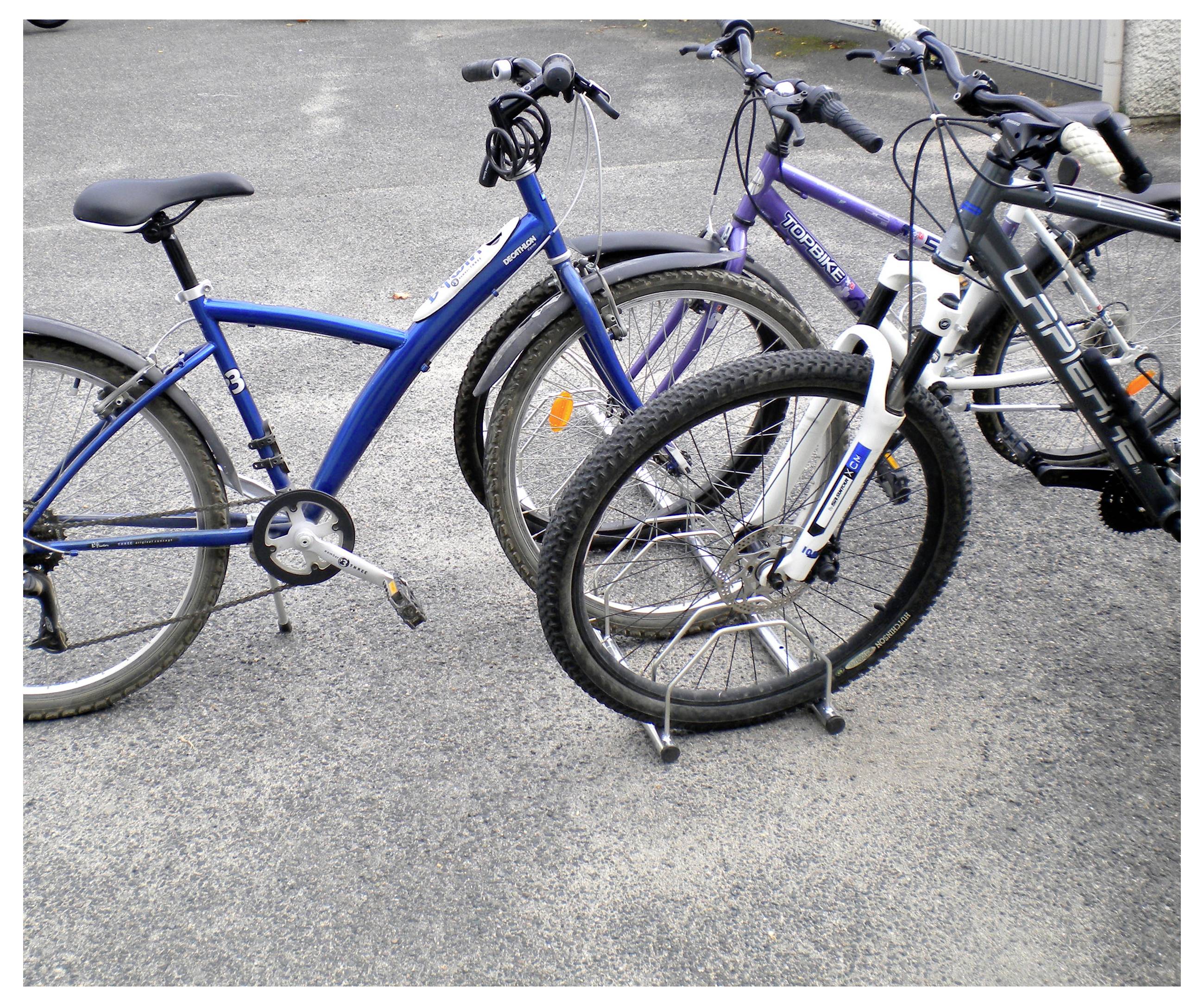 Flere cykler parkeret i et metalbikestativ på en belagt overflade, med en blå cykel i forgrunden.