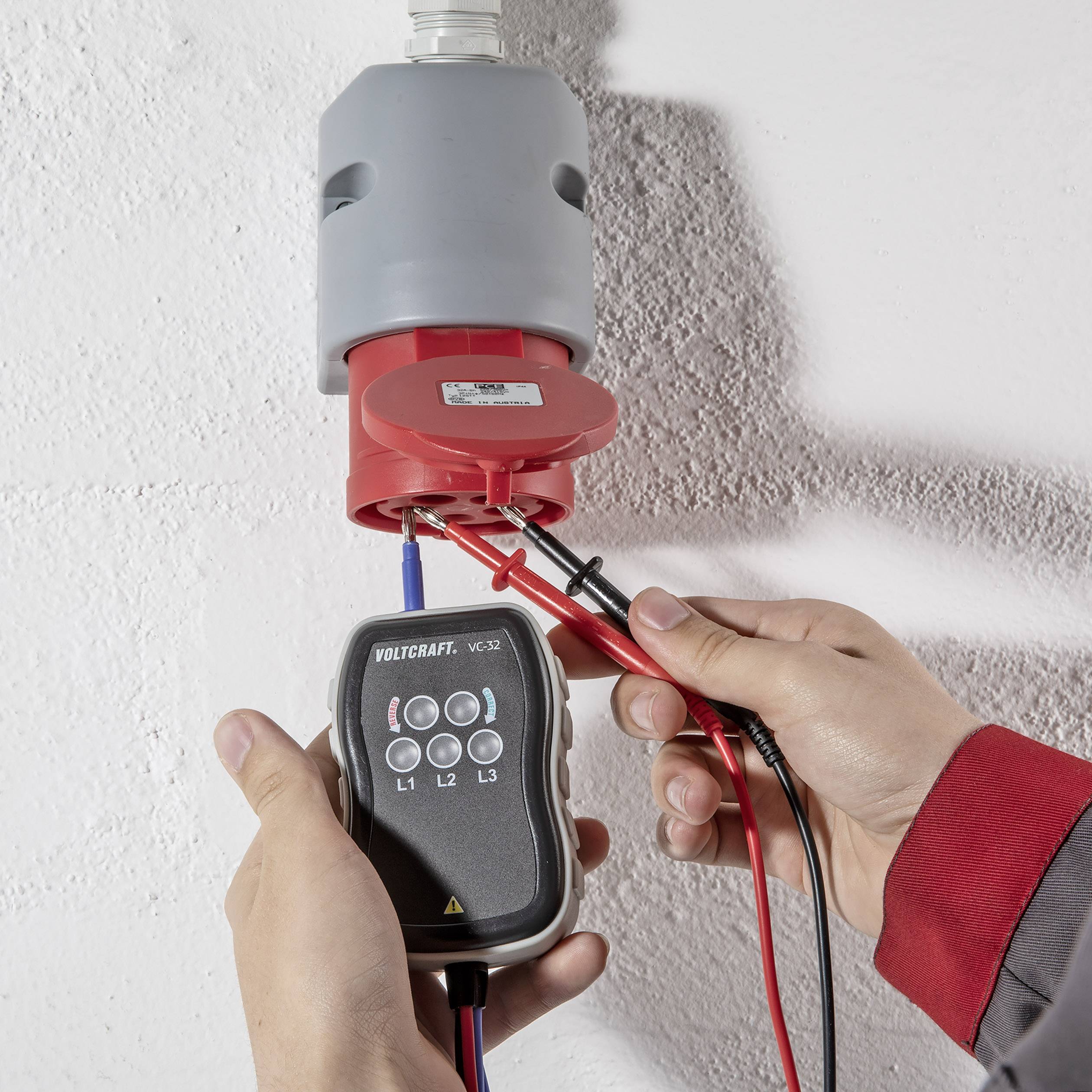 En tekniker bruger et voltmeter til at foretage elektriske målinger på en tre-ledet stikforbindelse.