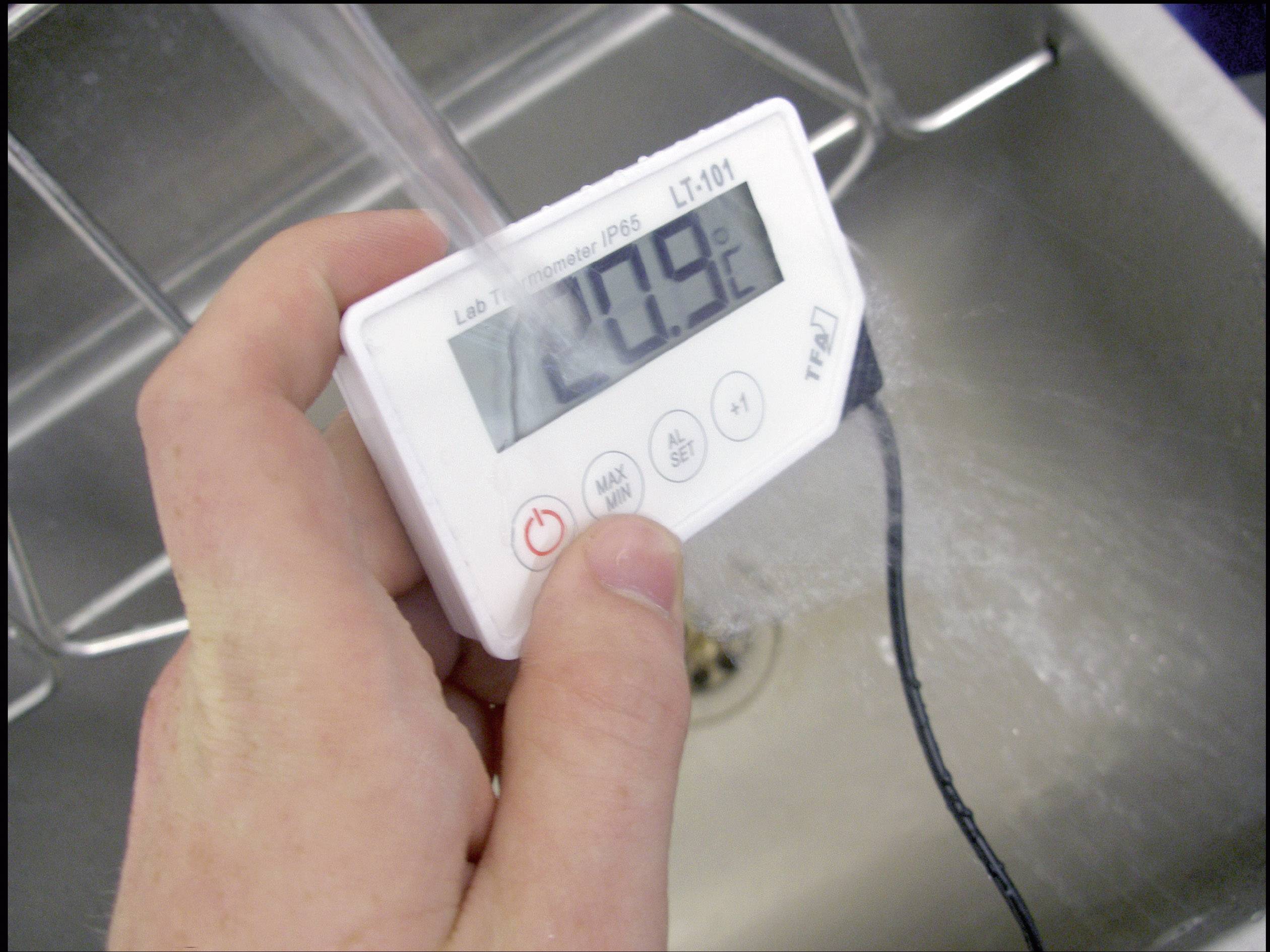 En hånd holder et digitalt termometer over et vaskebad, som viser 20,9 grader celsius. Vand løber henover.