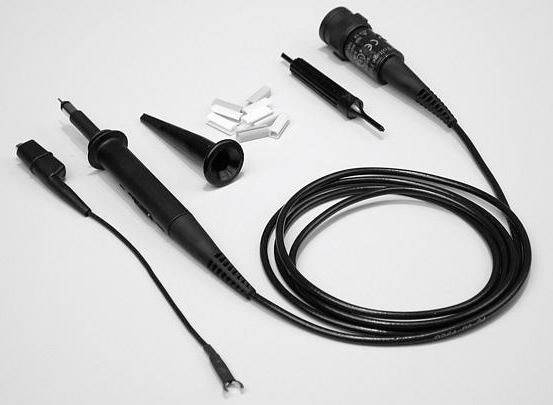 Et oscilloskop-målehovede med kabel, klemmer, adapter og konverteringsvedhæng liggende på et bord. Egnet til elektroniske målinger.
