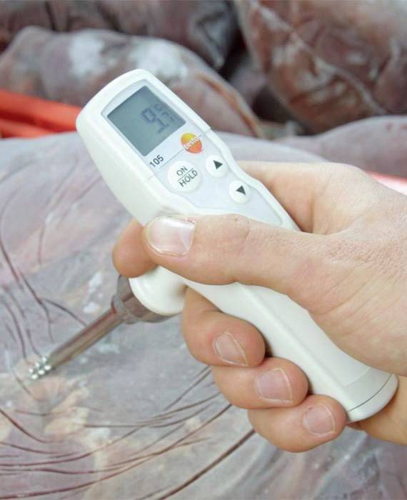 En hånd holder et fødevaregodkendt digitalt termometer, som er ført ind i et stykke kød. Displayet viser temperaturen.