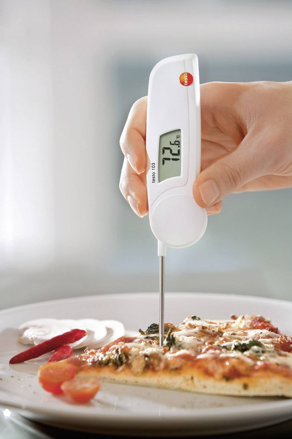 En hånd holder et digitalt termometer i en pizzaskive. Displayet viser 72,6 grader Celsius.