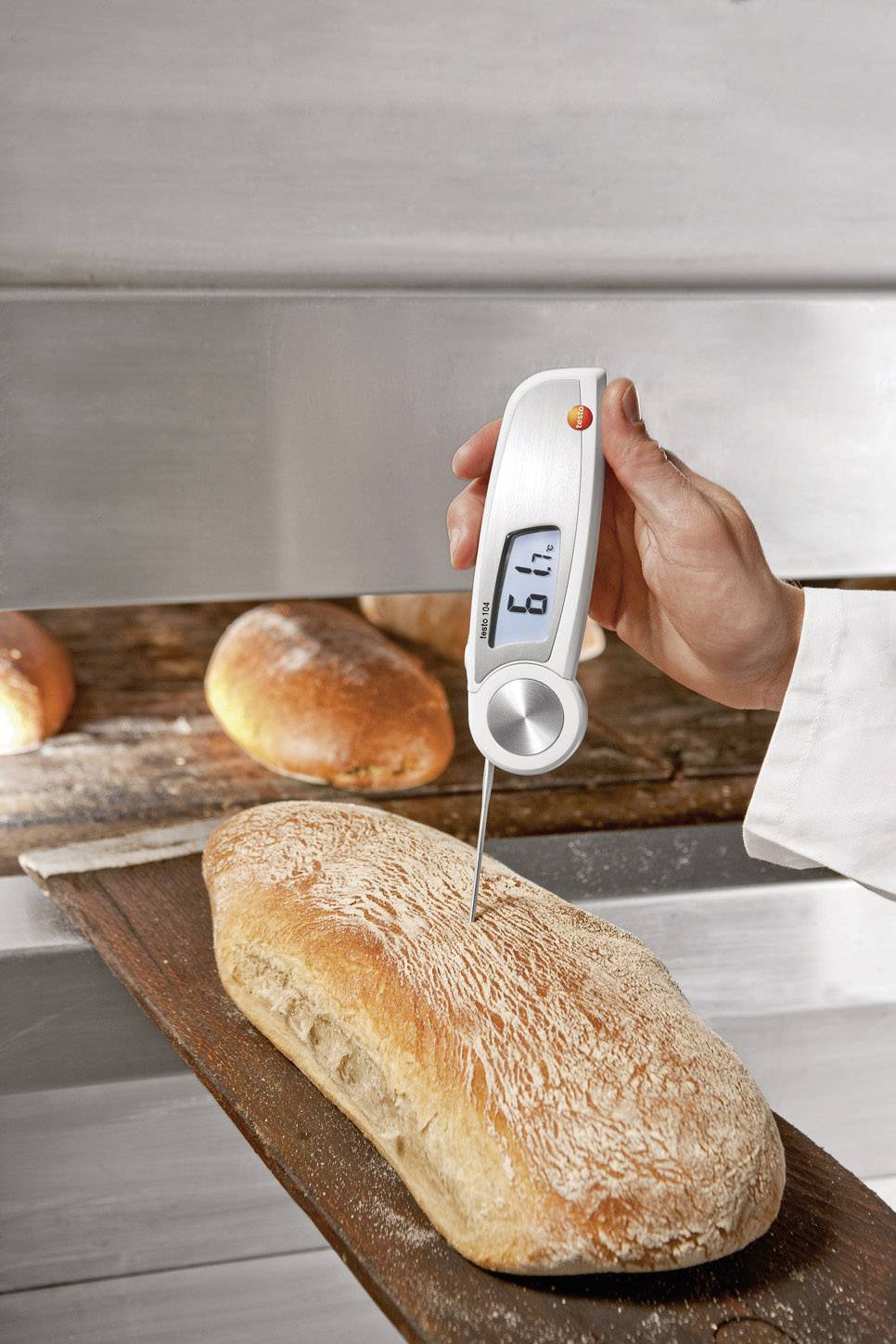 En person måler den indvendige temperatur i et nybagt brød med et digitalt termometer, der viser 16,7 grader.