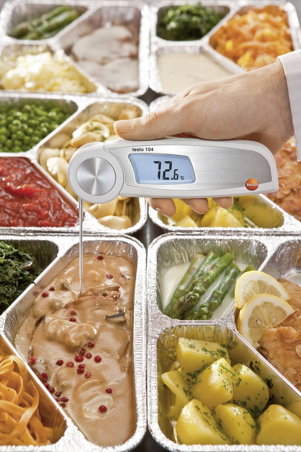 Et håndtermometer måler kerntemperaturen til 72,6°C i en aluminiumsskål med kyllingen, omgivet af forskellige retter.
