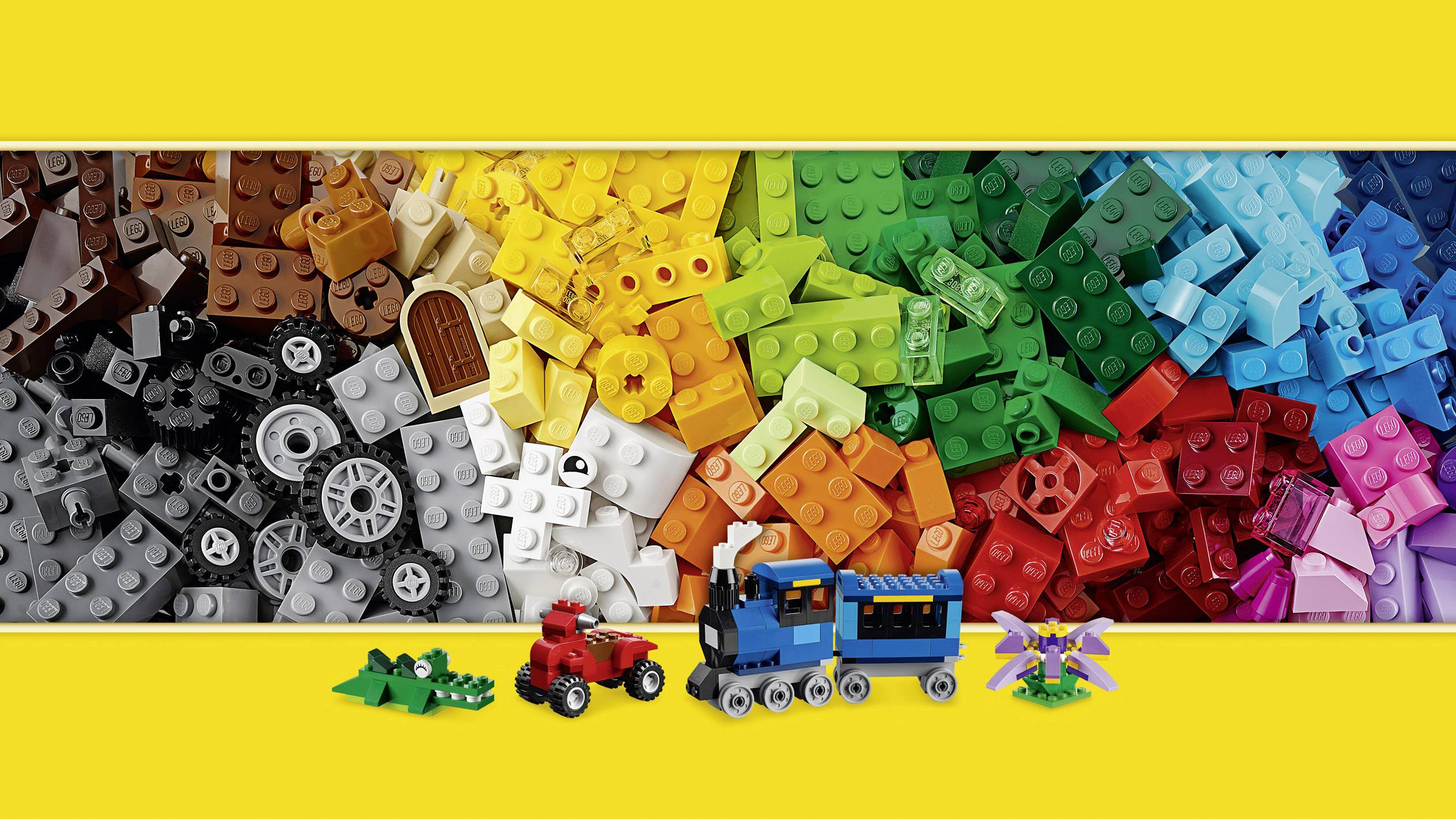 Farverige Lego-klodser arrangeret i en farvegradient fra sort til violet, med små Lego-figurer som et tog og et krokodille foran.