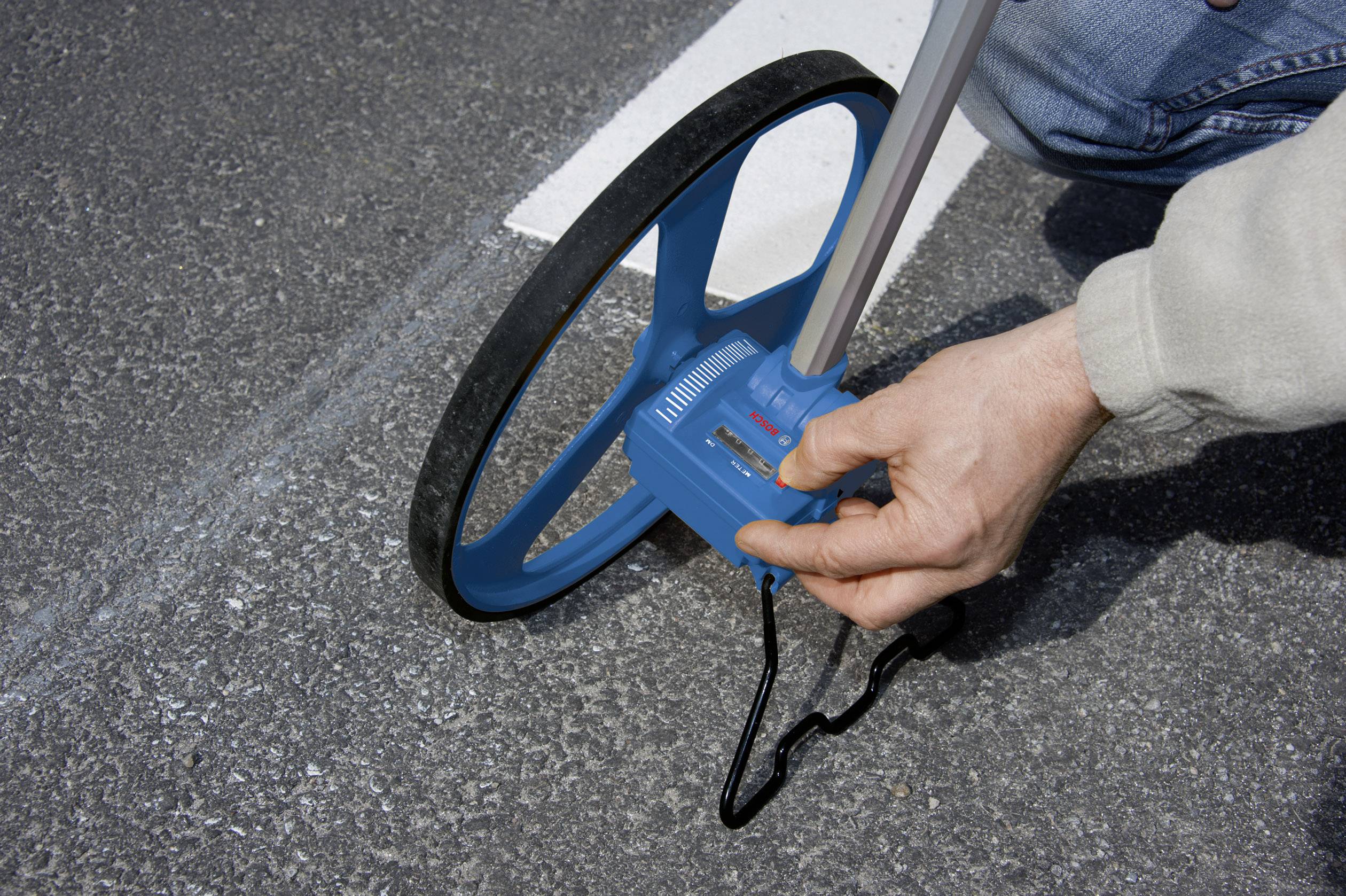 En person måler asfaltlængden langs en hvid linje ved hjælp af et målehjul.