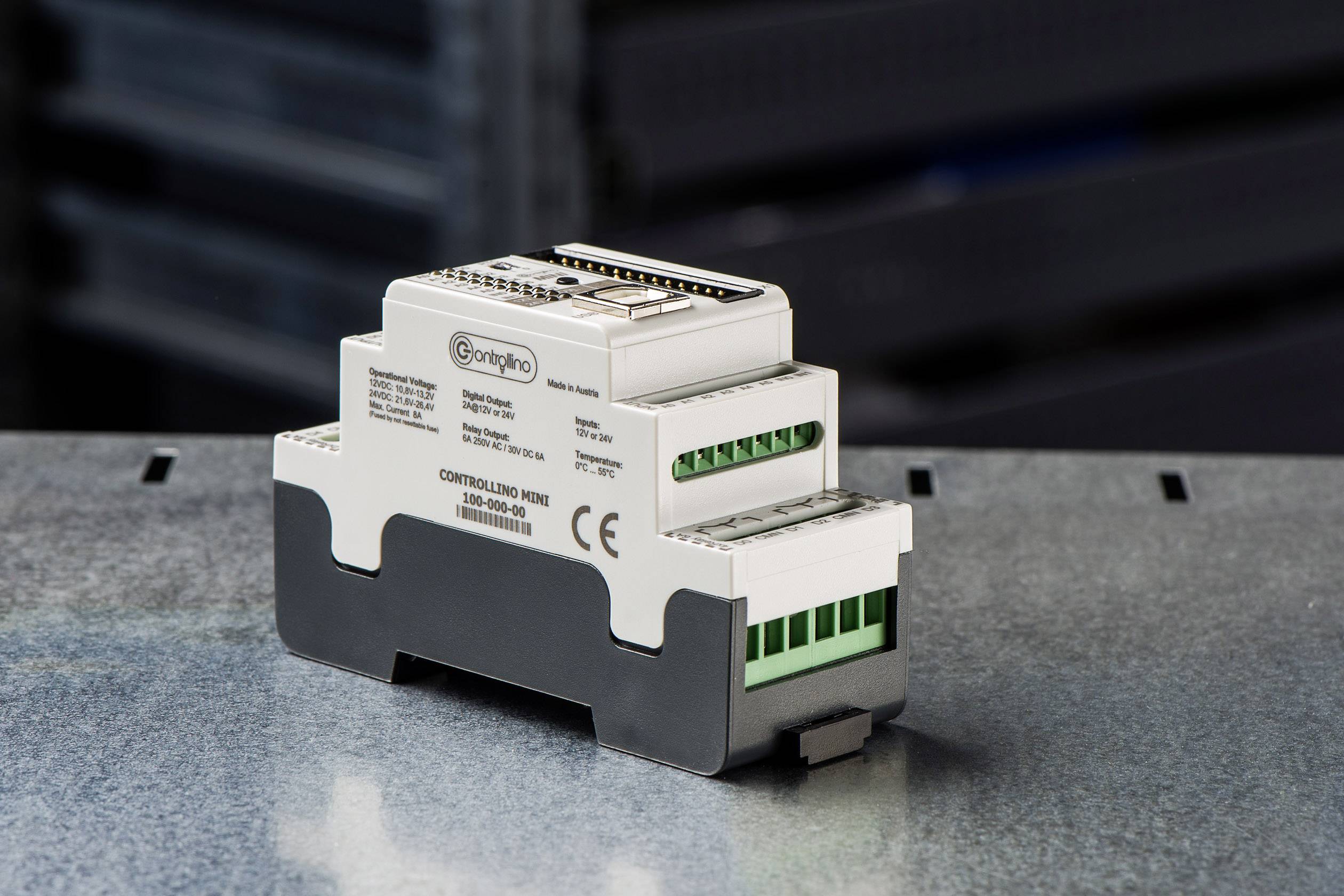 Et elektronisk styremodul med flere tilslutninger og CE-mærkning, placeret på en metaloverflade.