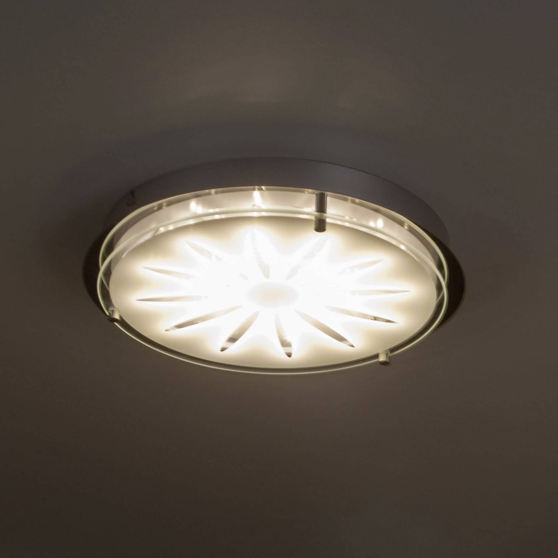 En lysende loftslampe med stråleformet mønster, der udsender diffust hvidt lys i rummet.