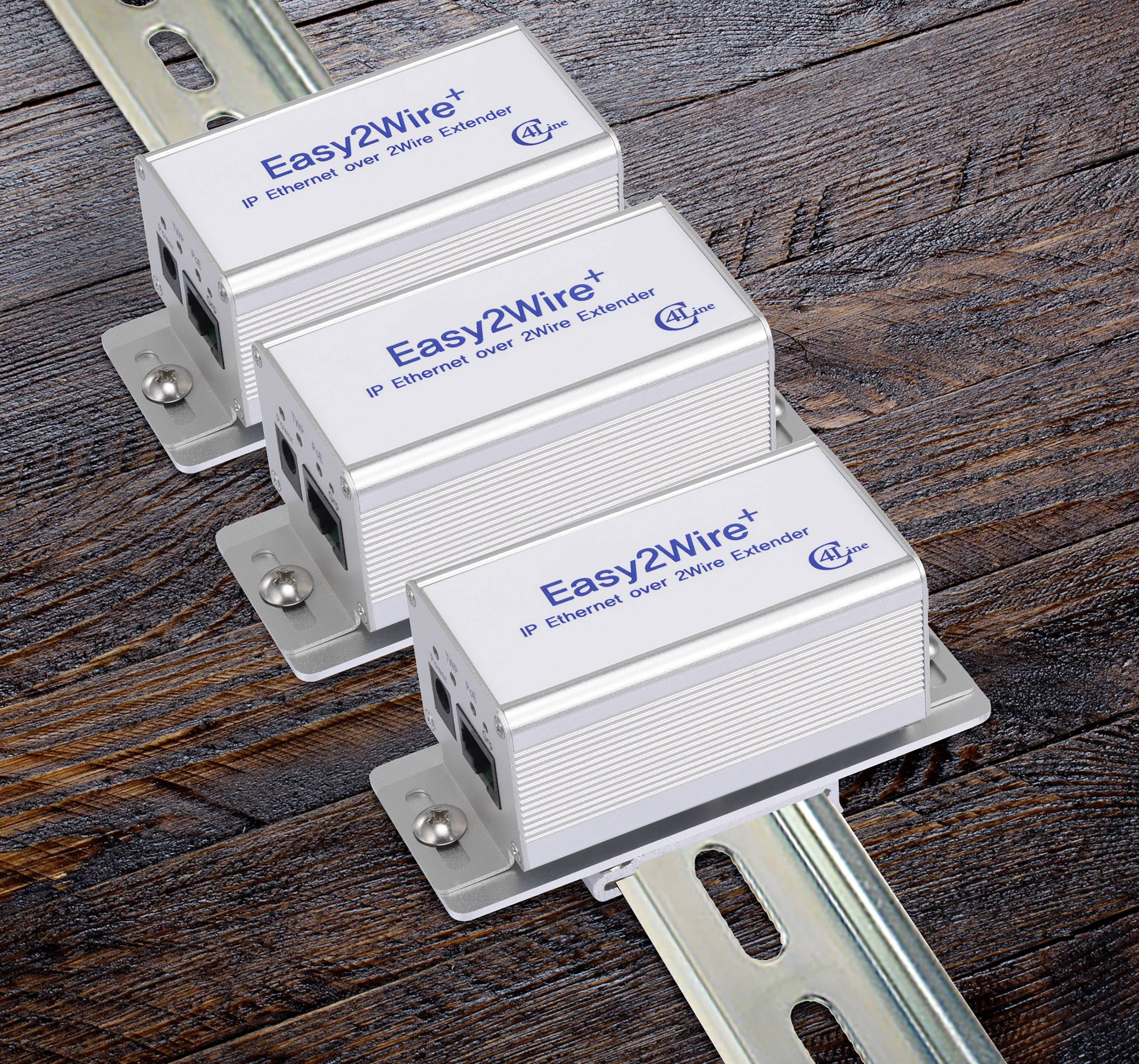 Tre 'Easy2Wire+' IP Ethernet-forlængere på træoverfladen, viser logo og funktion til Ethernet-udvidelse via tovejs-ledning.