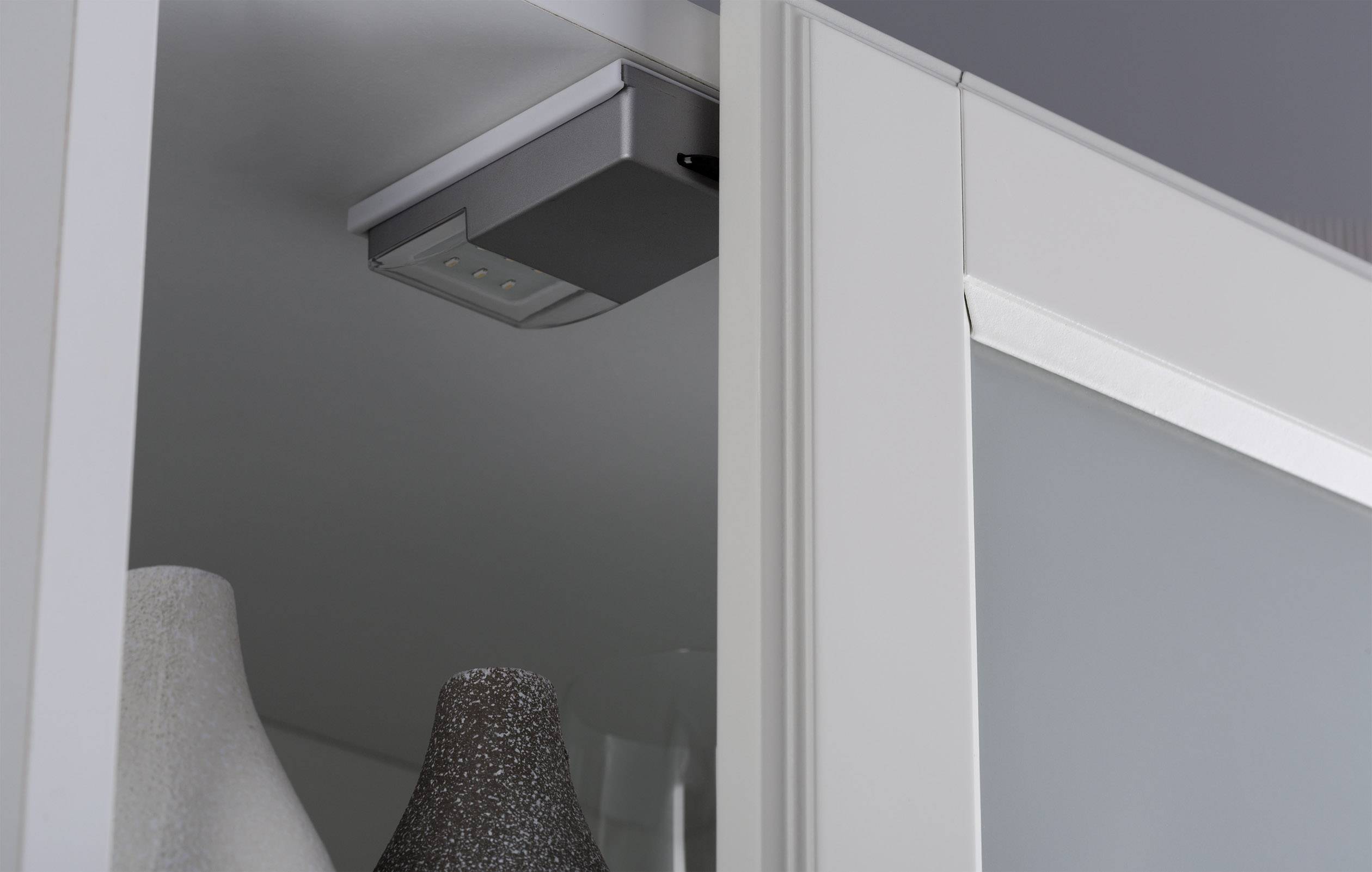 Et skab med en integreret LED-lampe langs indersiden af den øverste kant og vaser i baggrunden.