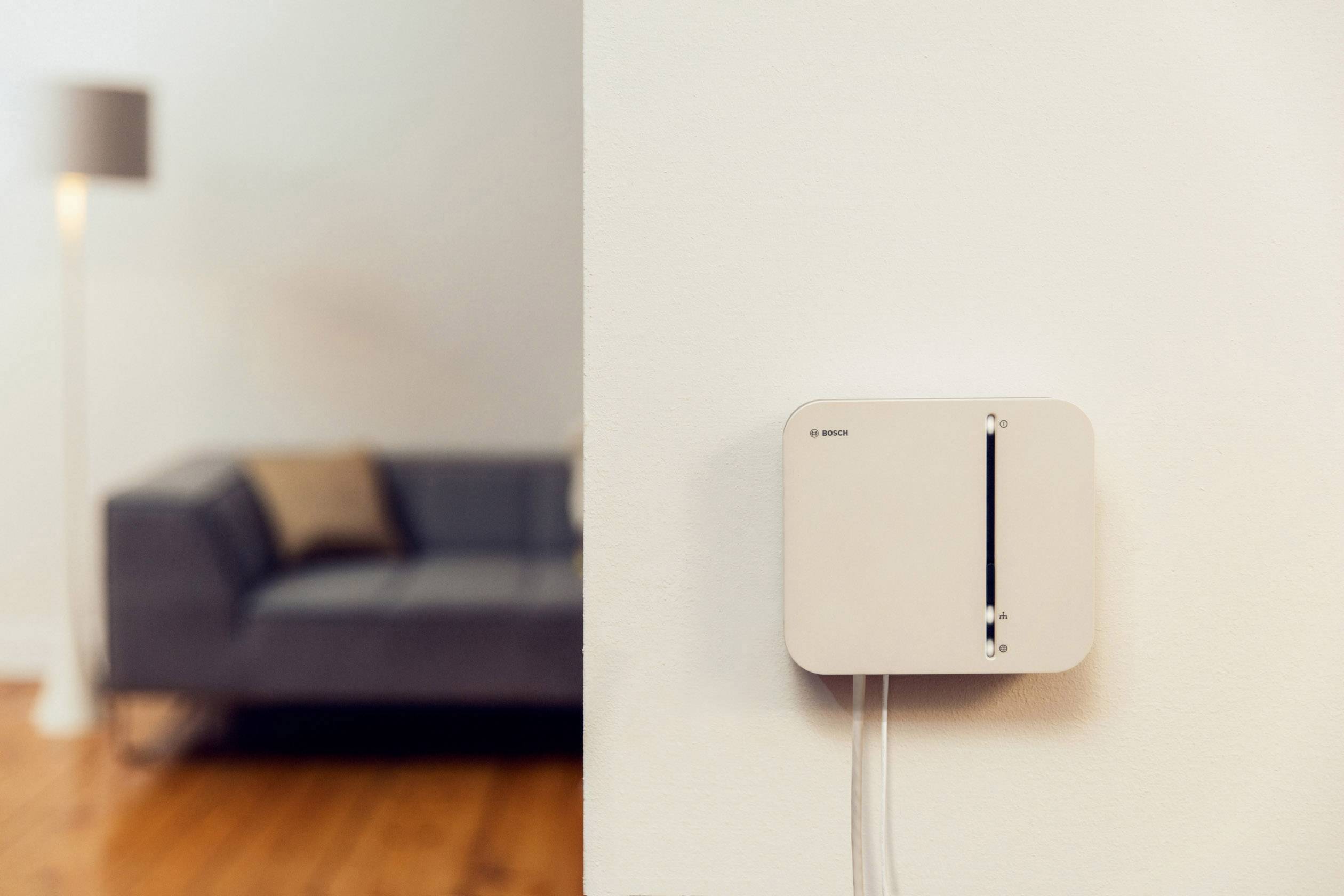 Hjemmeinventar med fokus på en moderne termostat på væggen; i baggrunden en grå sofa og en gulvlampe.
