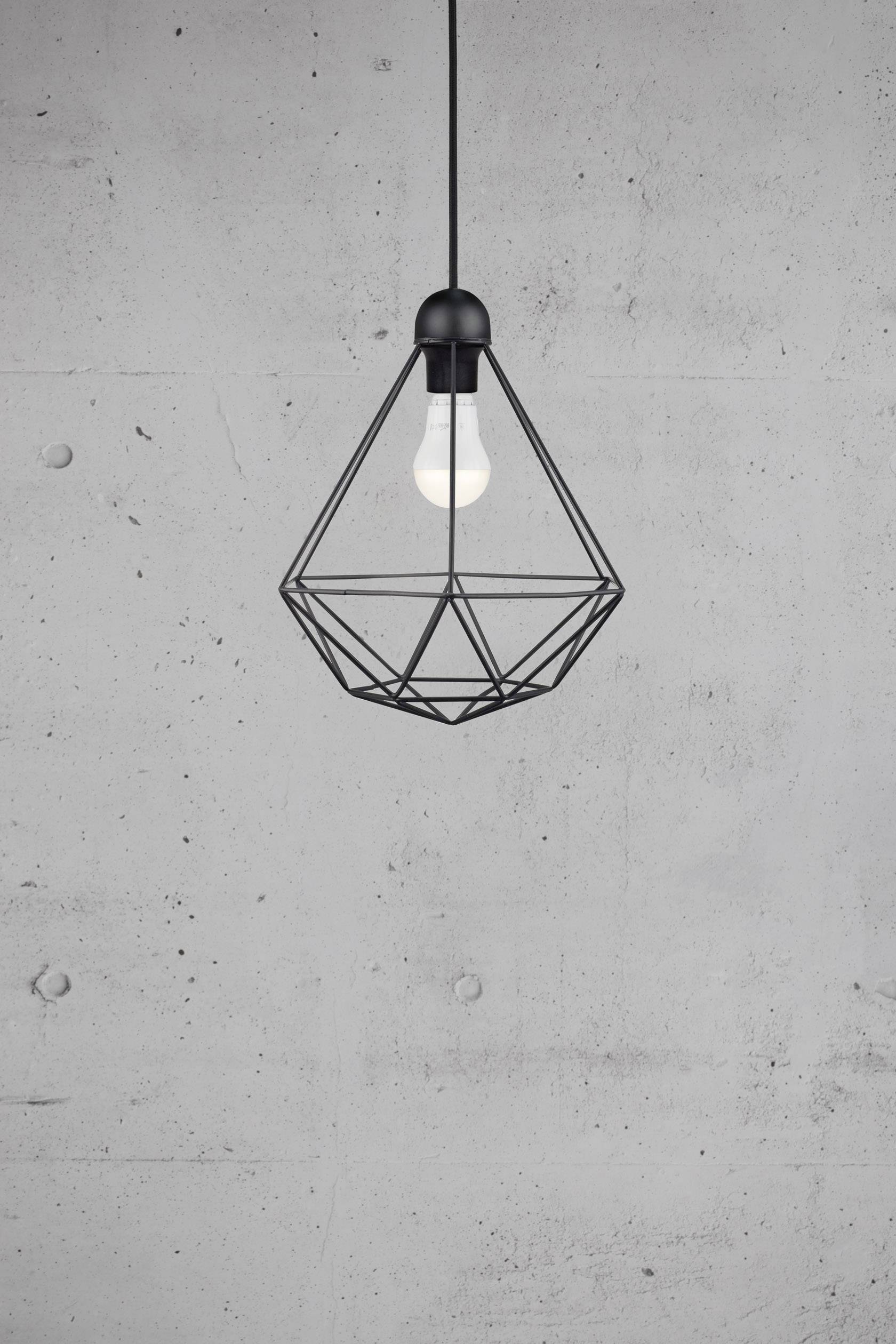 Moderne pendel med geometrisk design i sort metal hænger foran en grå betonvæg.