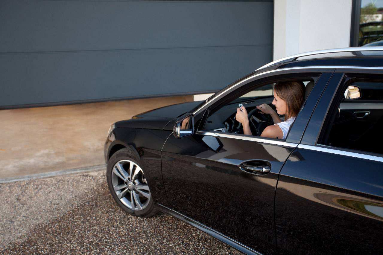 En kvinde sidder i en bil med sin smartphone foran en lukket garage port.