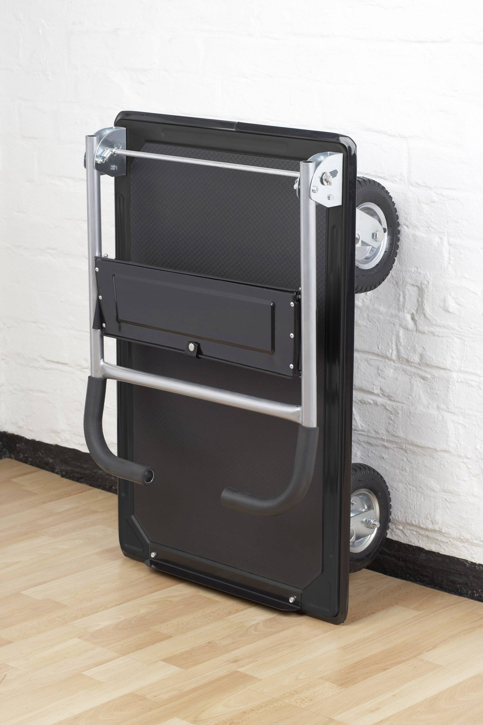 En sammenklappeligt transportvogn læner op ad en hvid murstenvæg på et trægulv.