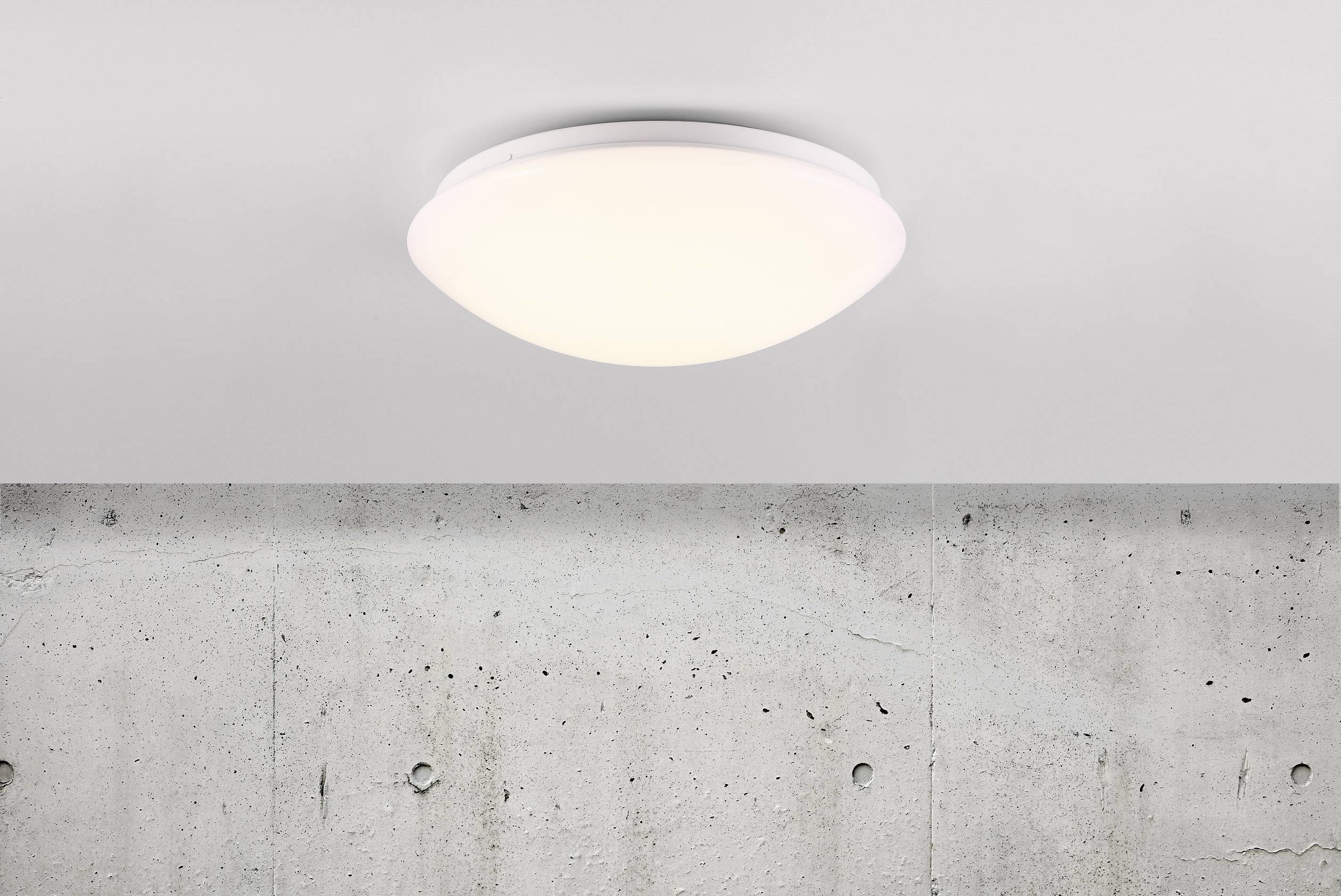 Rund, hvid loftslampe lyser op mod en grå betonvæg.