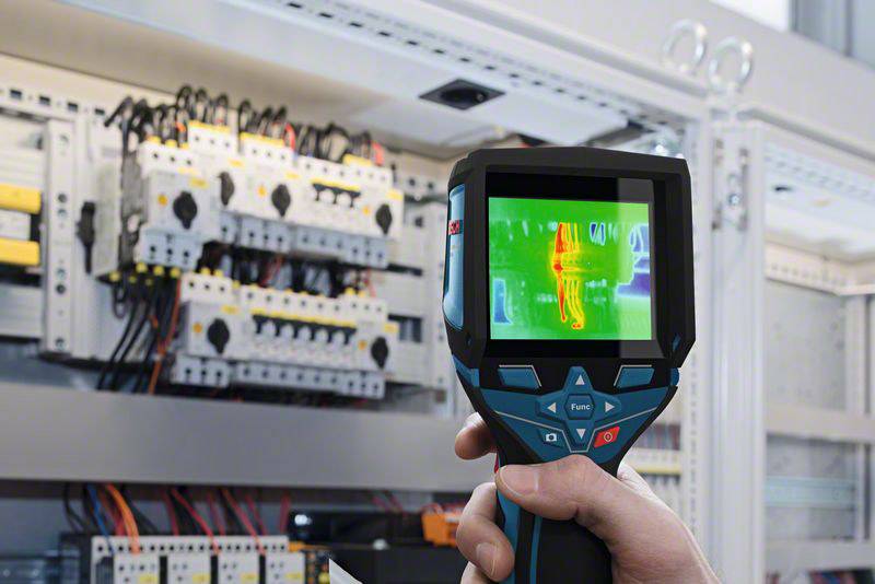 En hånd holder et varmekamera foran et åbnet el-skab. Skærmen viser farvet varmefordeling af de elektriske komponenter.