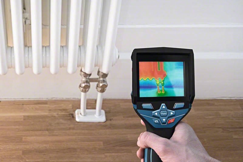 En person holder et termisk kamera, der viser temperaturforskelle på en radiator. Identificerer varmetab eller ineffektiviteter.