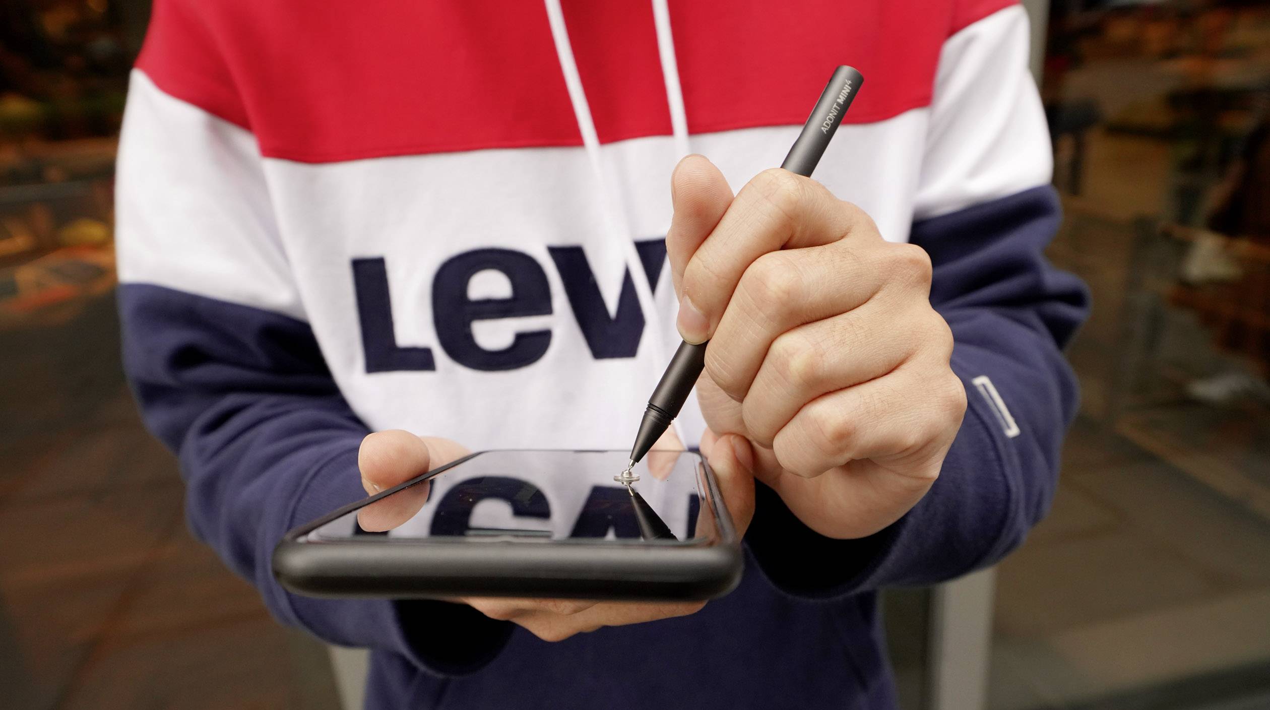 En person holder en smartphone i den ene hånd og bruger en stylus til at skrive eller tegne på skærmen.