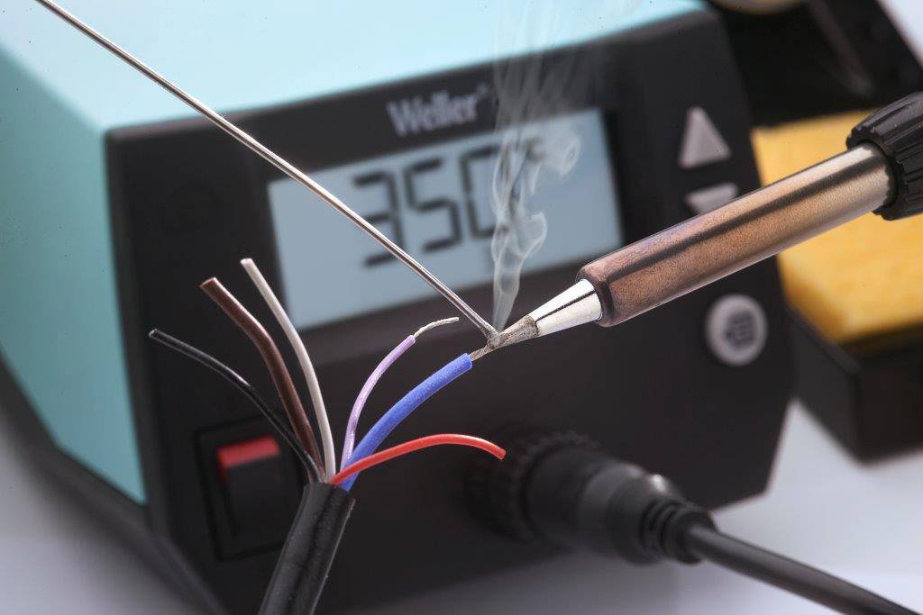 Loddekolben opvarmer en ledning ved siden af styringsenheden med displayet '250°'. Forskellige kabelender er synlige og viser elektronisk arbejde.