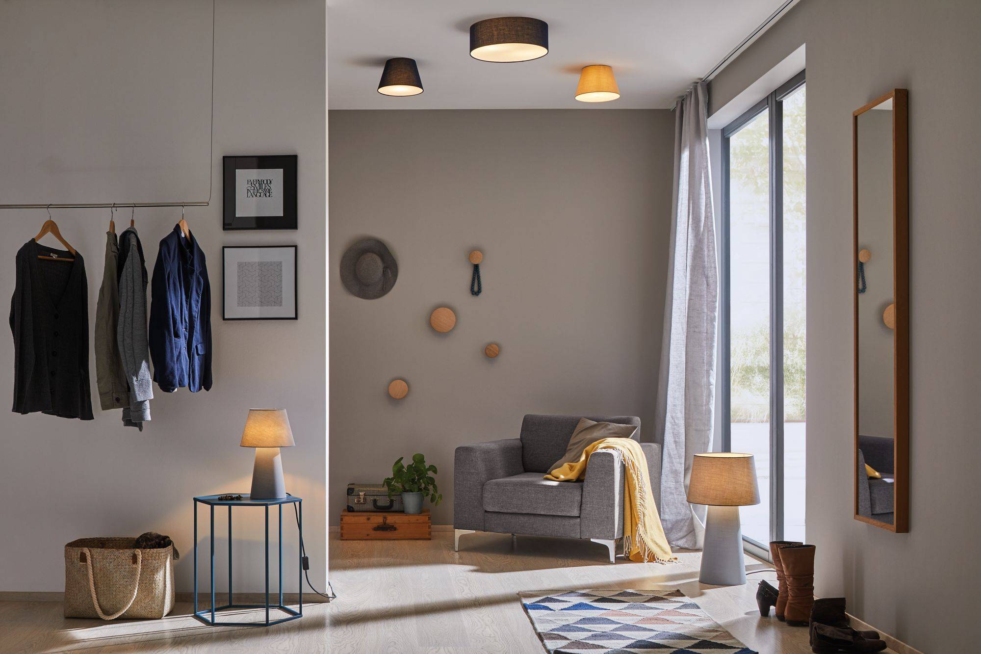 Et moderne stue med en grå lænestol, en standerlampe og vægkunst. Et stort spejl reflekterer dagslys fra et stort vindue.