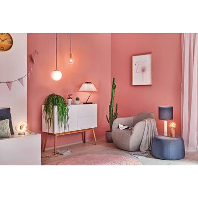Et hyggeligt stue med lyserøde vægge, en lænestol og planter. En kommode med en lampe og hængende belysning supplerer rummet.