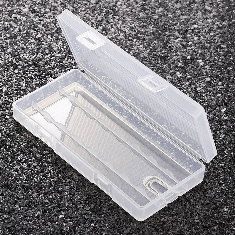 En gennemsigtig, åben plastboks ligger på en mørk, kornet overflade. Boksen har rum og er tom.