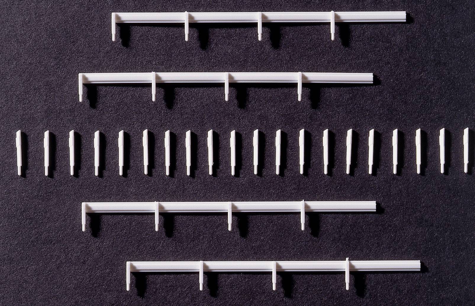 Hvide plastik-clips og rawplugs jævnt arrangeret på sort baggrund, mange på en række, andre i grupper.