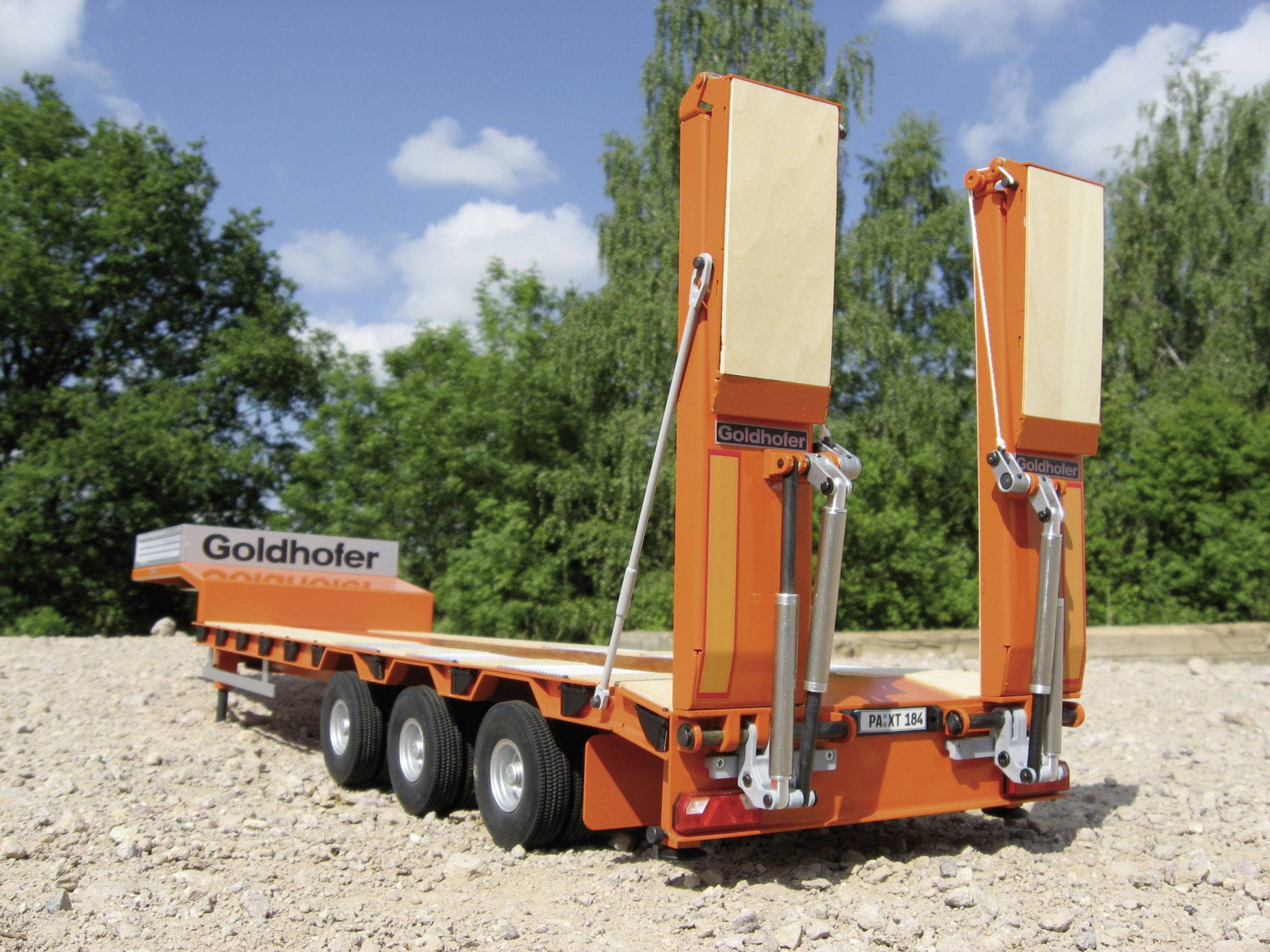 En orange sværgodstrailer fra mærket Goldhofer holder på en grusflade foran en baggrund af grønne træer.