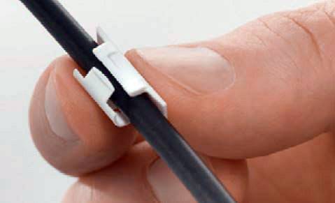 En hånd holder et sort kabel med en lille, hvid kabelclips påsat. Clippsen organiserer og fastgør kablet.