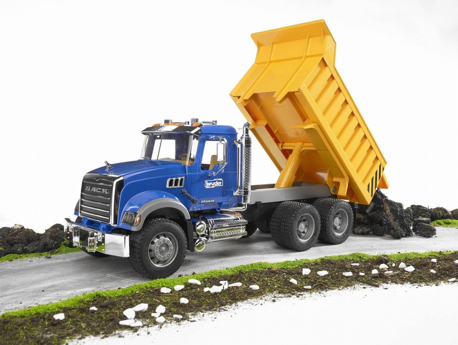 En blå legetøjslastbil med gul tippelad tipper sten ud på en vej. Lastbilen er detaljeret og står på en grøn baggrund.