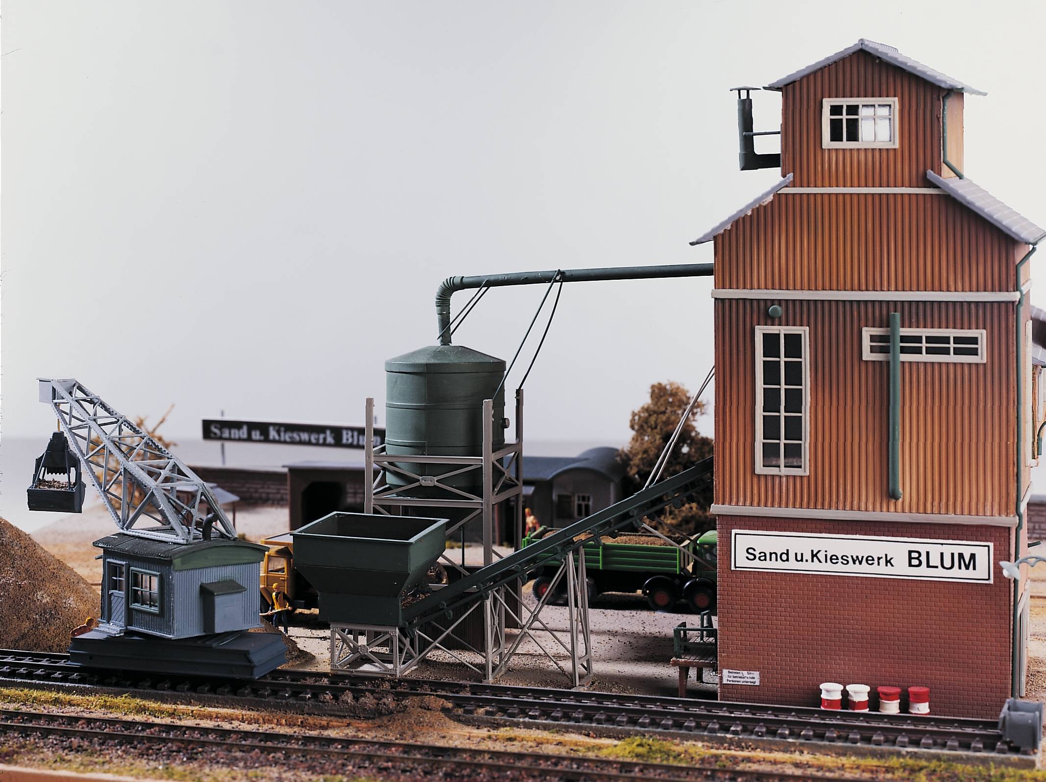 En modeltogsscene med et sand- og grusgravværk, herunder et transportbånd, siloer og en kran. Bygningen er mærket 'Sand & Grusgrav Blum'.
