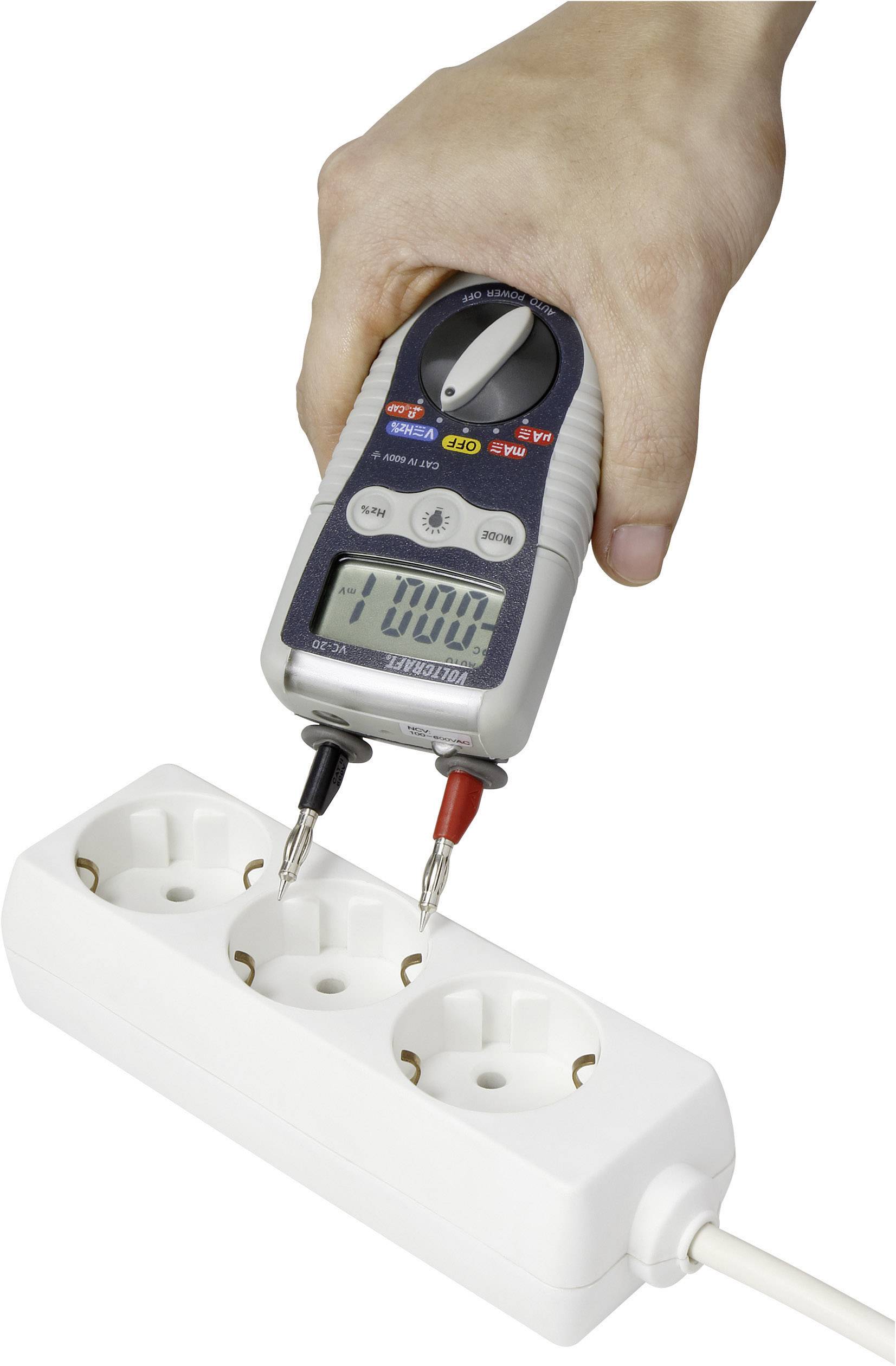 En hånd holder et multimeter, der måler strømforbruget i et stikdåsefelt. Displayet viser '0.000'.