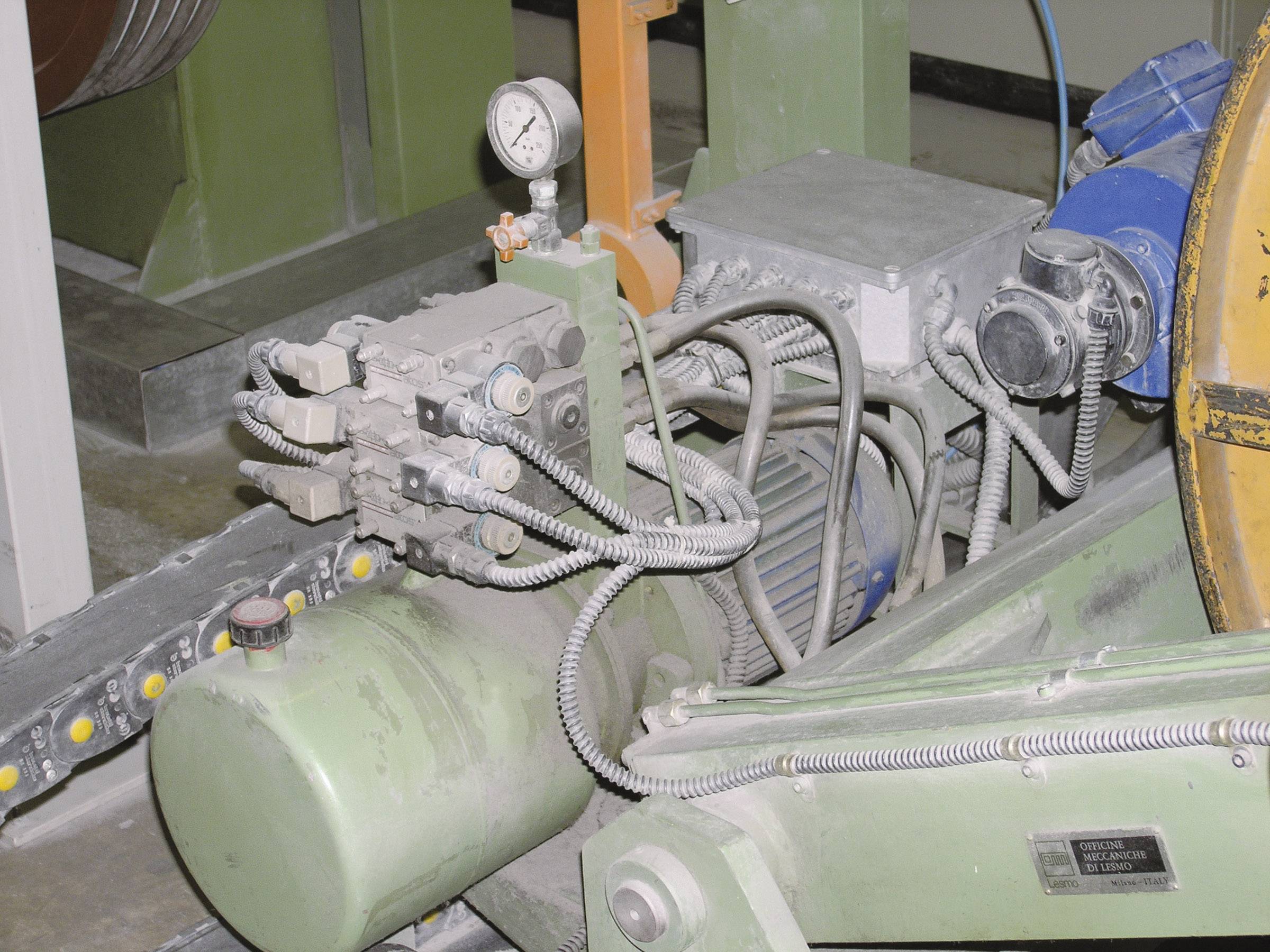 Industriel maskine med hydraulikcylinder og manometer, viser komponenter i et produktionssystem. Kabler og slanger er synlige.