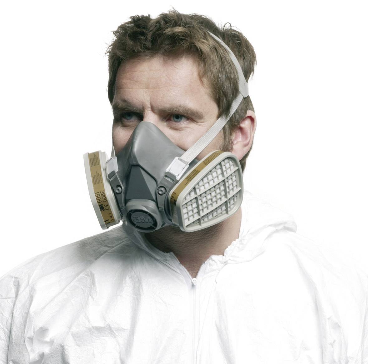 En person i beskyttelsesdragt bærer en åndedrætsmaske med filtre. Personen kigger til siden.