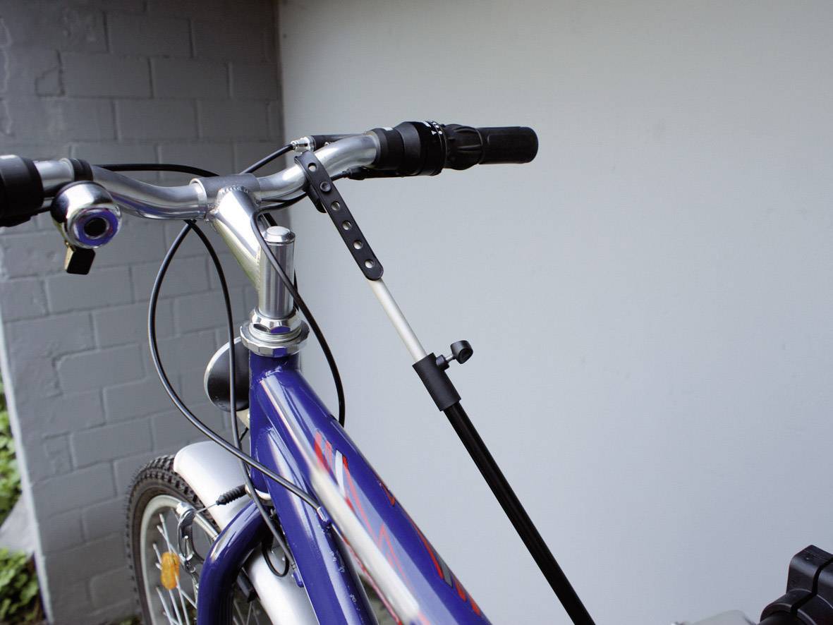 Nærbillede af en blå cykel med sort styr og monteret støtteben, lænet op ad en husmur.