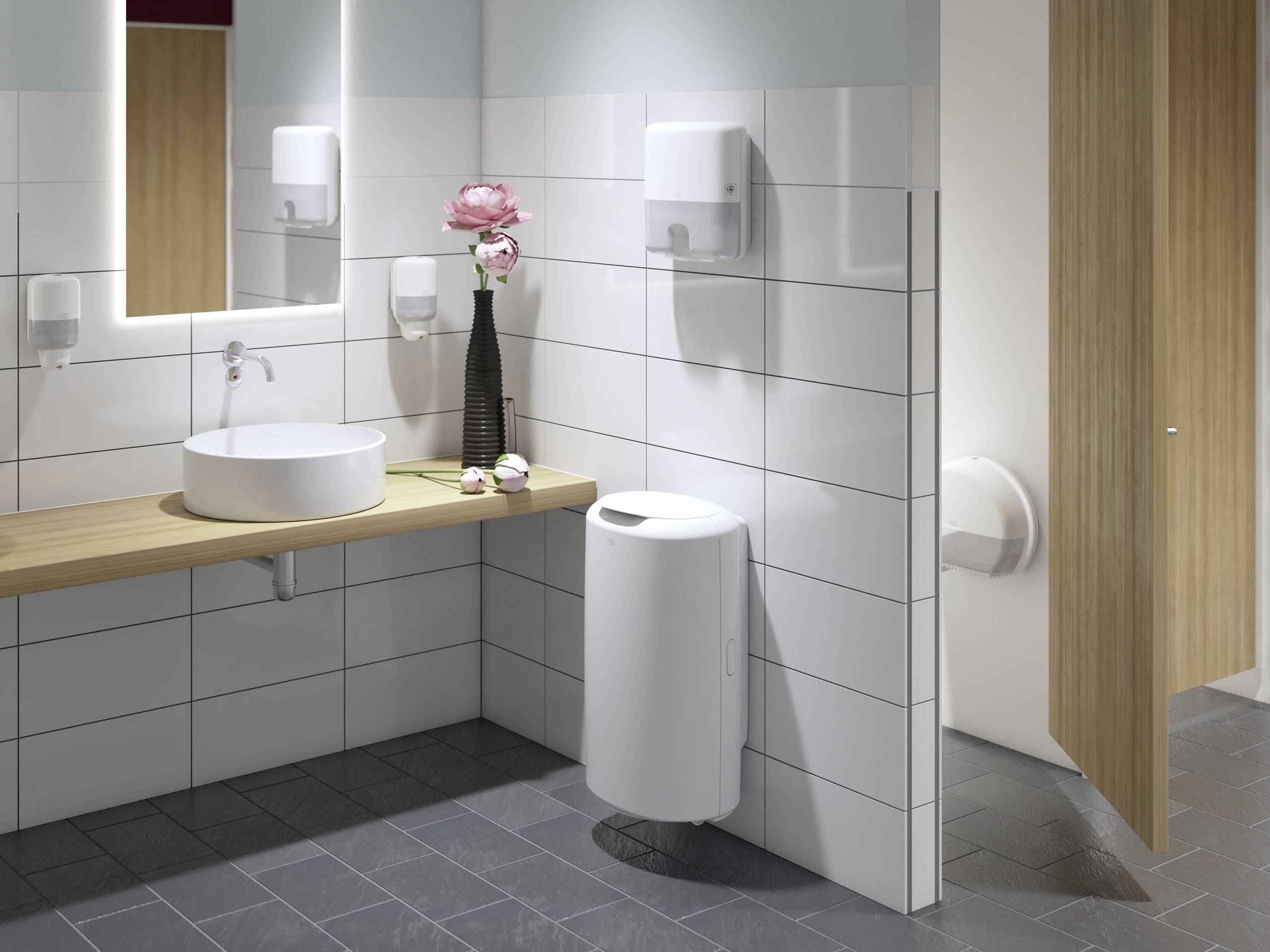 Moderne badeværelse med vask, spejl, håndklædeholder og vase med rosa blomst på træhylde. Døren til toilettet er delvist åben.