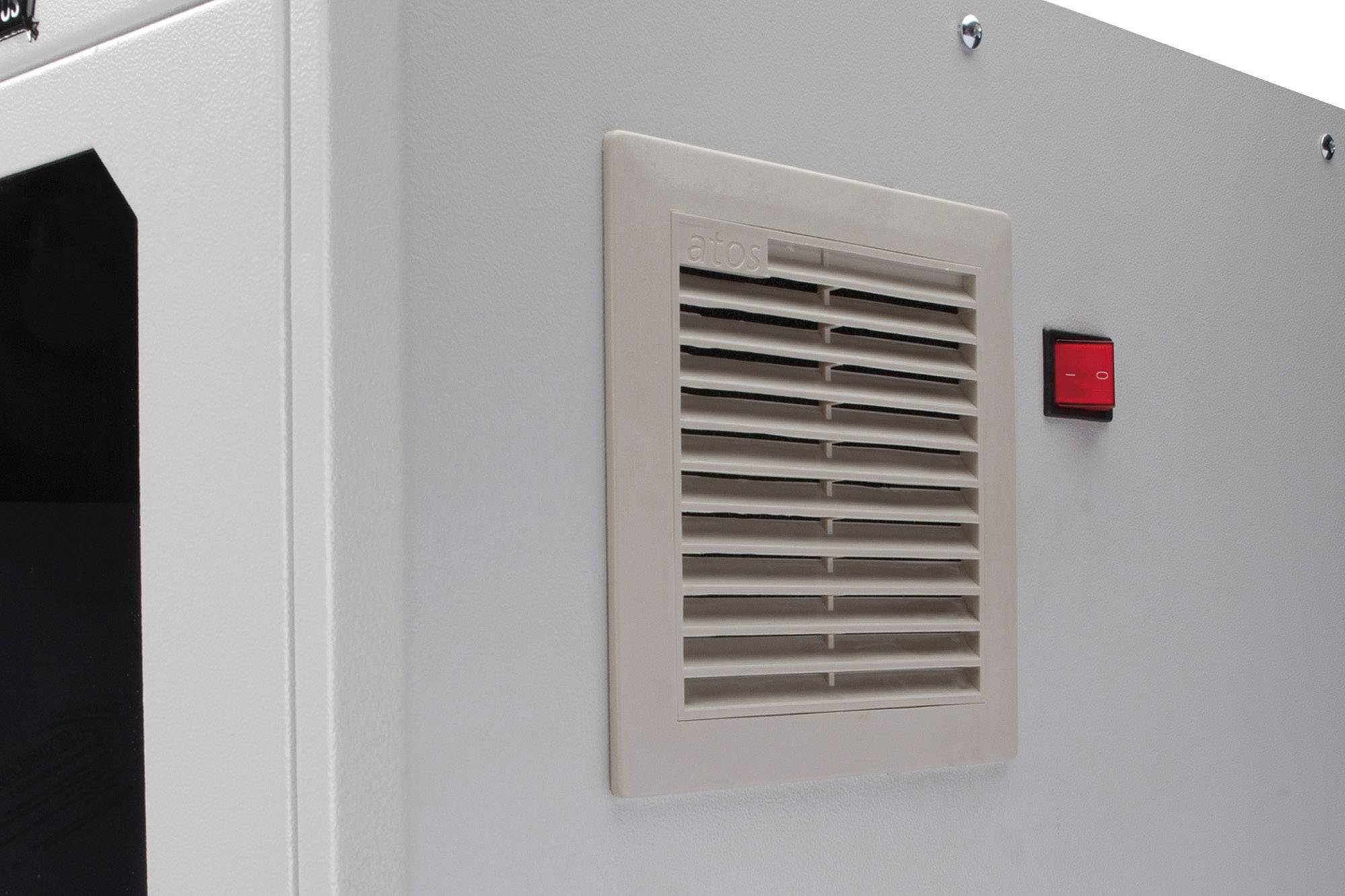 Et gråt kabinet med et rektangulært ventilationsgitter og en lille, rød kontakt.