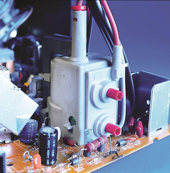 Elektronikplatine mit verschiedenen elektronischen Bauteilen, darunter Kondensatoren, Widerstände und Kabel, die an einem zentralen Anschlussblock angeschlossen sind.