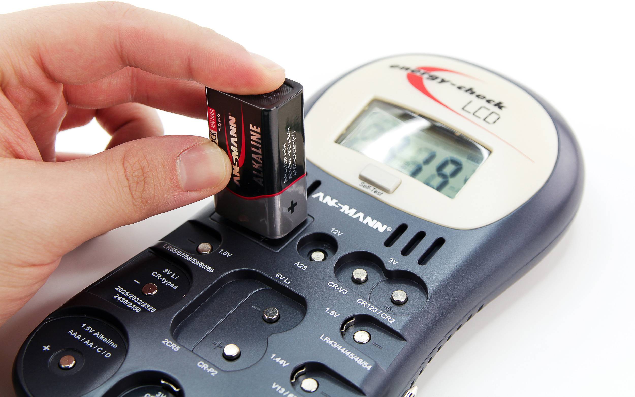 Eine Hand testet eine Batterie mit einem digitalen Batterietester. Der Bildschirm zeigt den Ladezustand der Batterie an.
