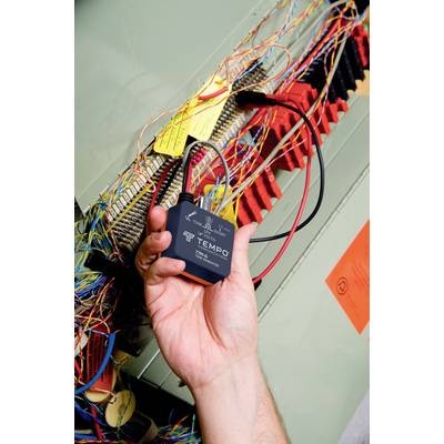 Hand hält ein elektrisches Prüfgerät mit Kabeln in einem Schaltschrank. Bunte Drähte und Etiketten sind sichtbar.