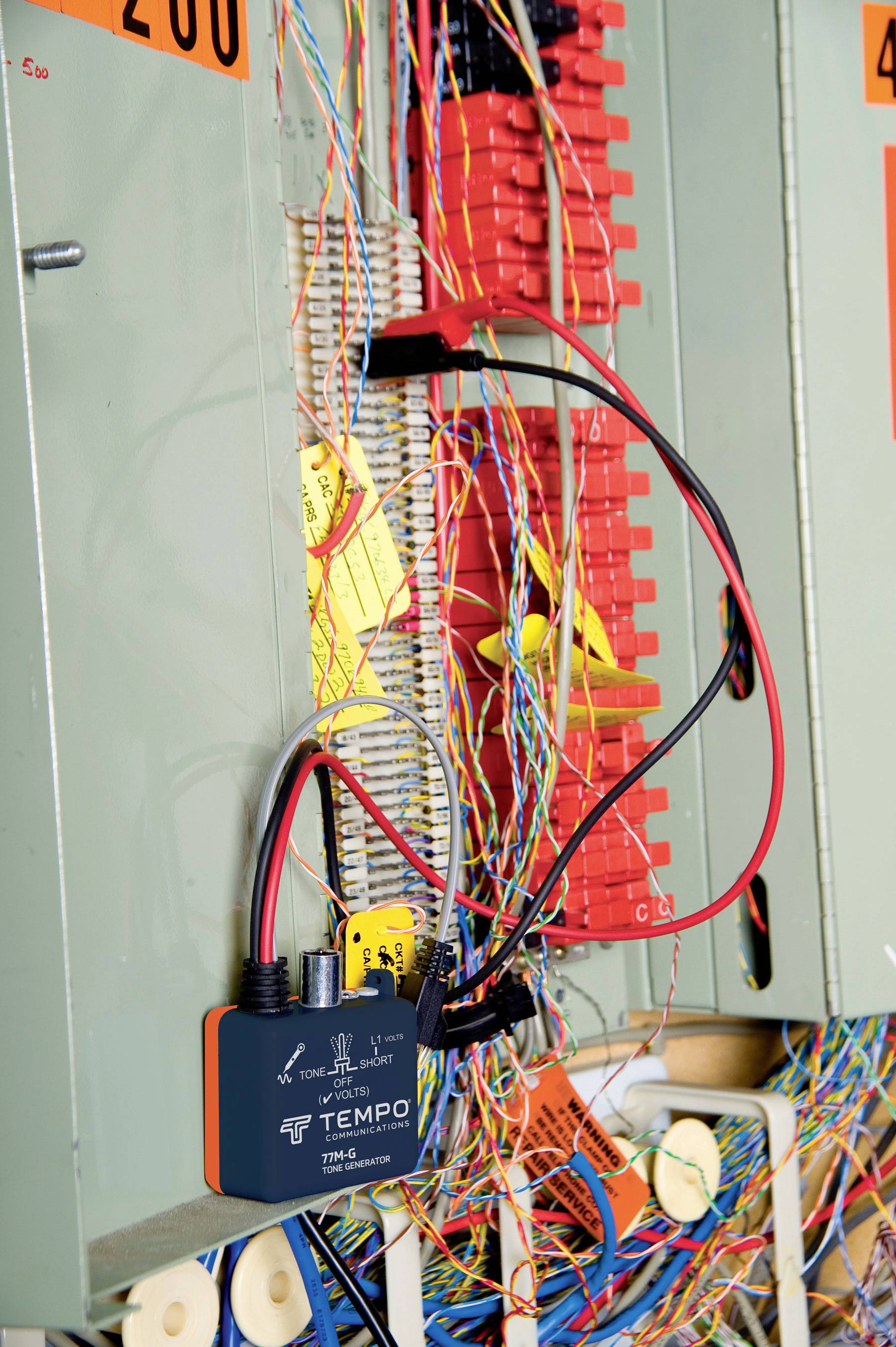Ein Schaltschrank mit vielen bunten Drähten und einem Gerät von Tempo. Einige Drähte sind mit gelben Etiketten markiert.