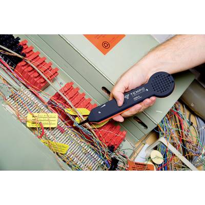 Hand hält ein Prüfgerät an einem Telefonkabel in einem Verteilerkasten. Verschiedene farbige Kabel sind zu sehen.