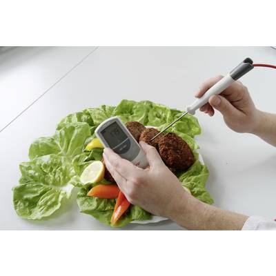 Person misst mit Thermometer die Temperatur von Frikadellen auf Salatblatt mit Paprika und Zitrone auf Tisch.