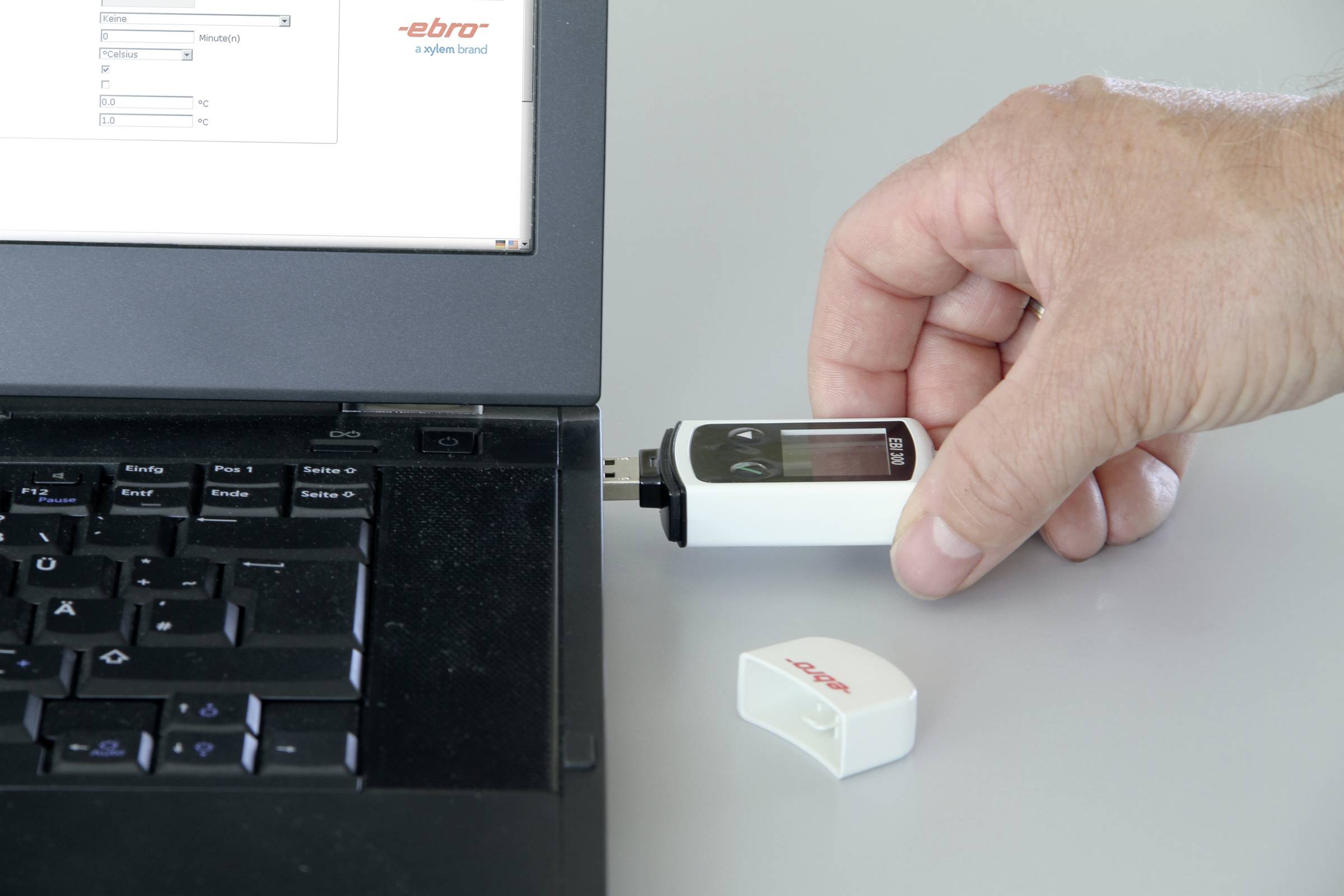 Eine Person steckt ein USB-Gerät an einen Laptop an. Auf dem USB-Gerät und daneben liegenden Deckel steht 'ebro'.